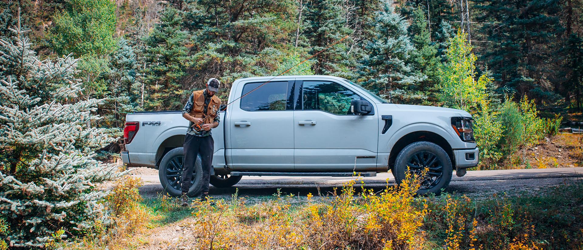 Man with a fishing pole stands in front of a 2025 Ford F-150® truck in a wooded area