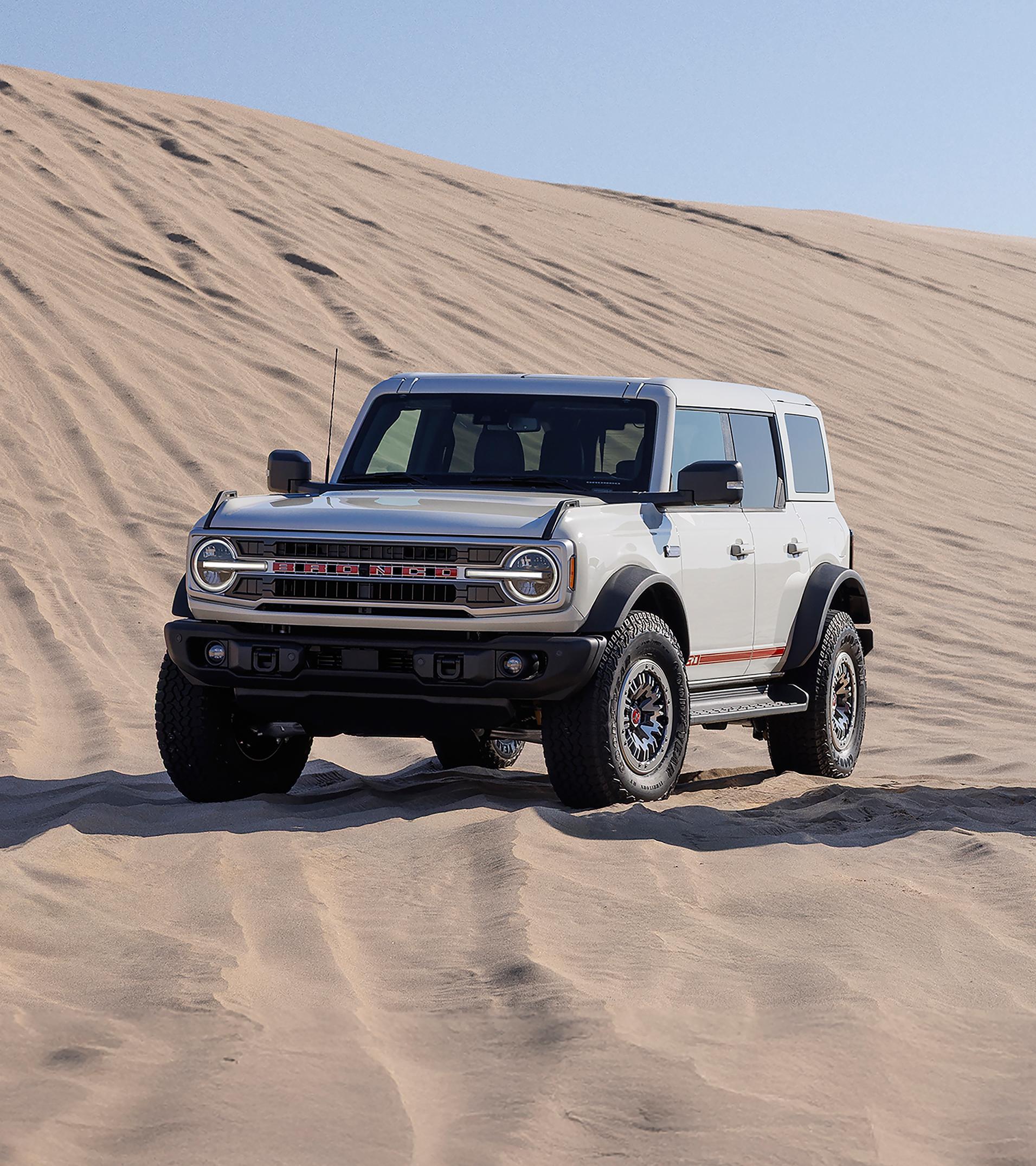 Two 2026 Ford Bronco® Outer Banks® SUVs with the available 60th Anniversary Package, parked on a sand dune