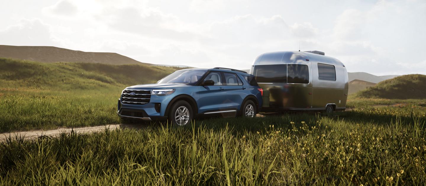 A 2025 Ford Explorer® SUV tows a camper on a path beside a field