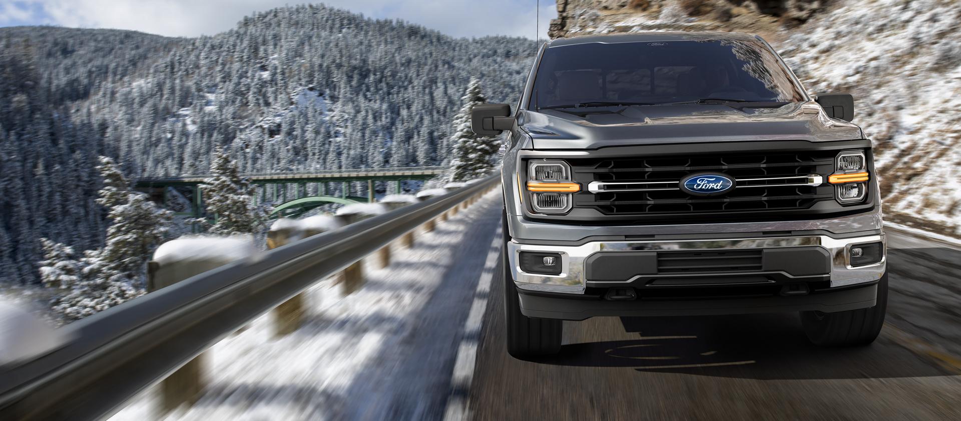 2026 Ford F-150® Lariat® model being driven on a mountain roadway with snow-covered mountains