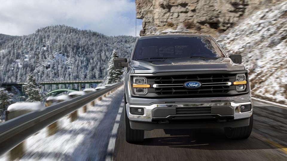 2026 Ford F-150® Lariat® model being driven on a mountain roadway with snow-covered mountains