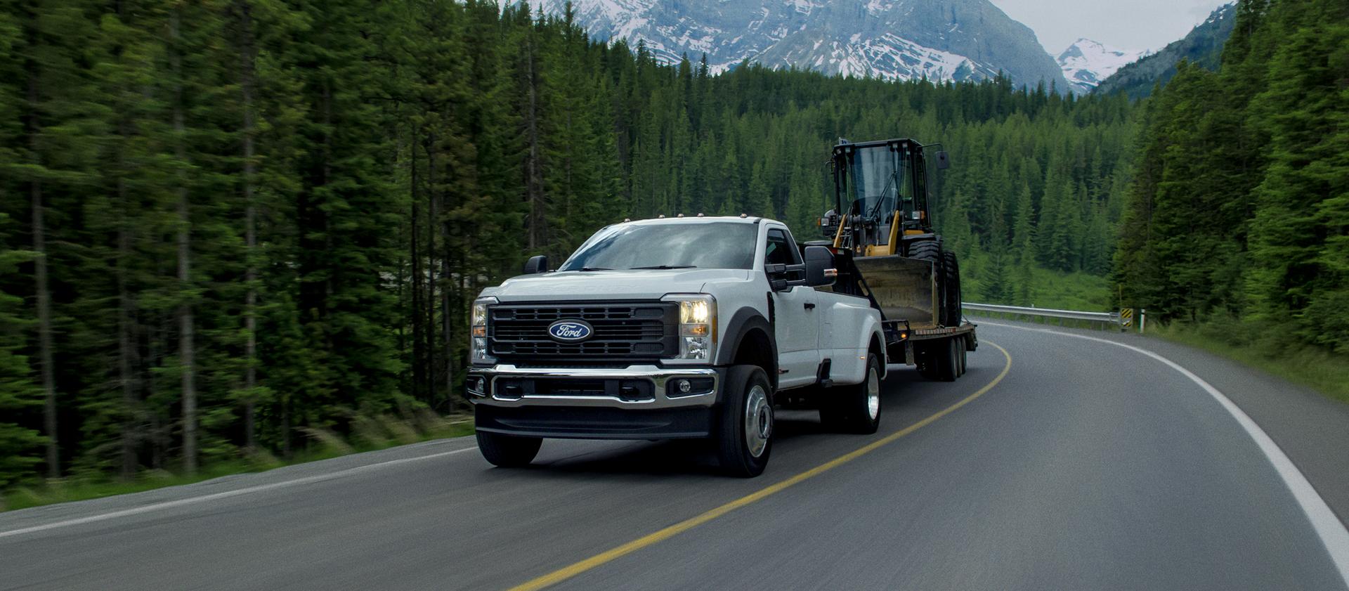 2027 Ford Super Duty® F-450® XL model towing a large flatbed trailer carrying a compact wheel loader