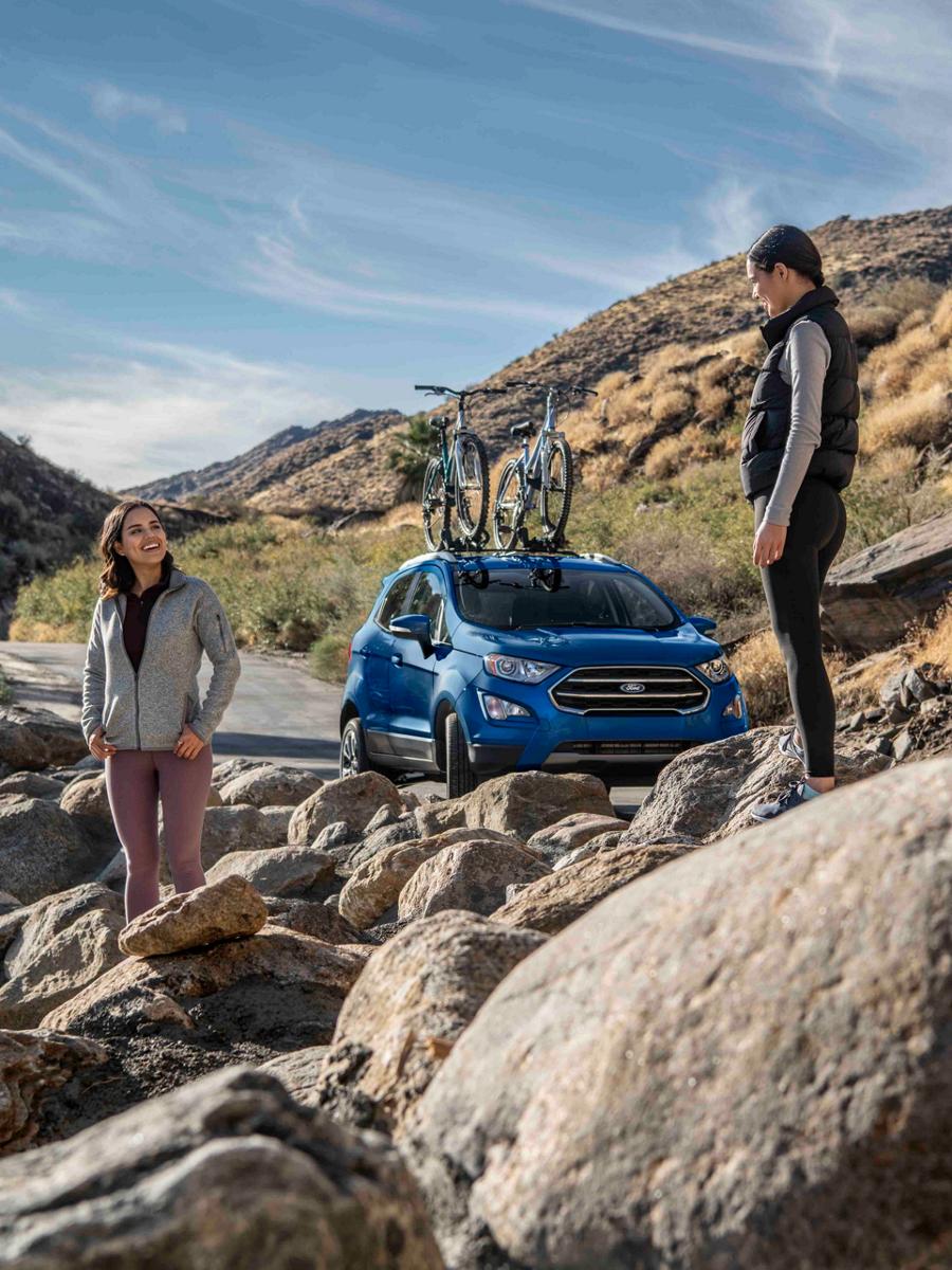 Two young women stand in a rocky landscape near a Ford crossover