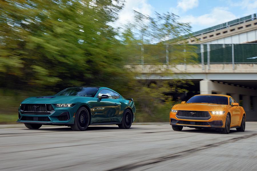 Two Ford Mustangs driving side by side near an overpass