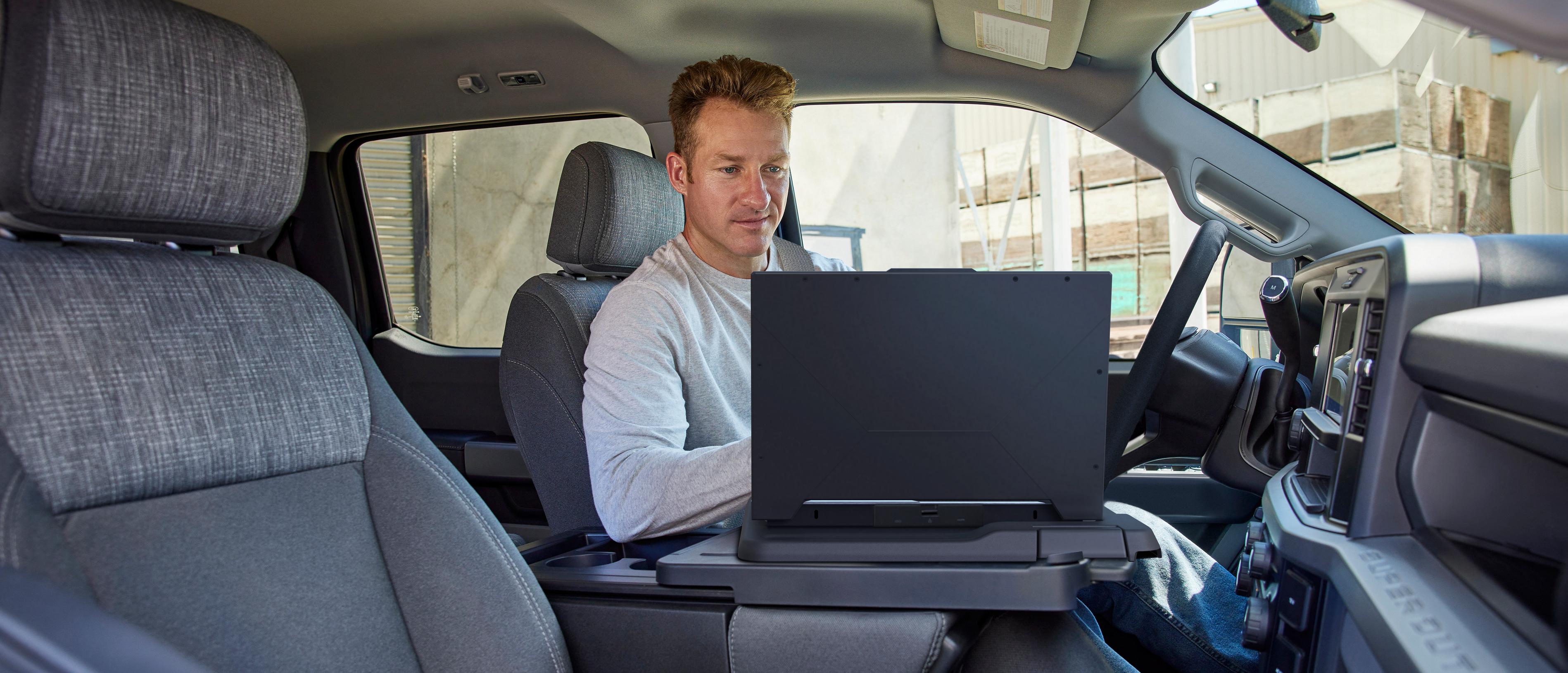 Person seated inside a parked 2026 Ford Super Duty® F-250® XL pickup using a laptop with the interior work surface feature