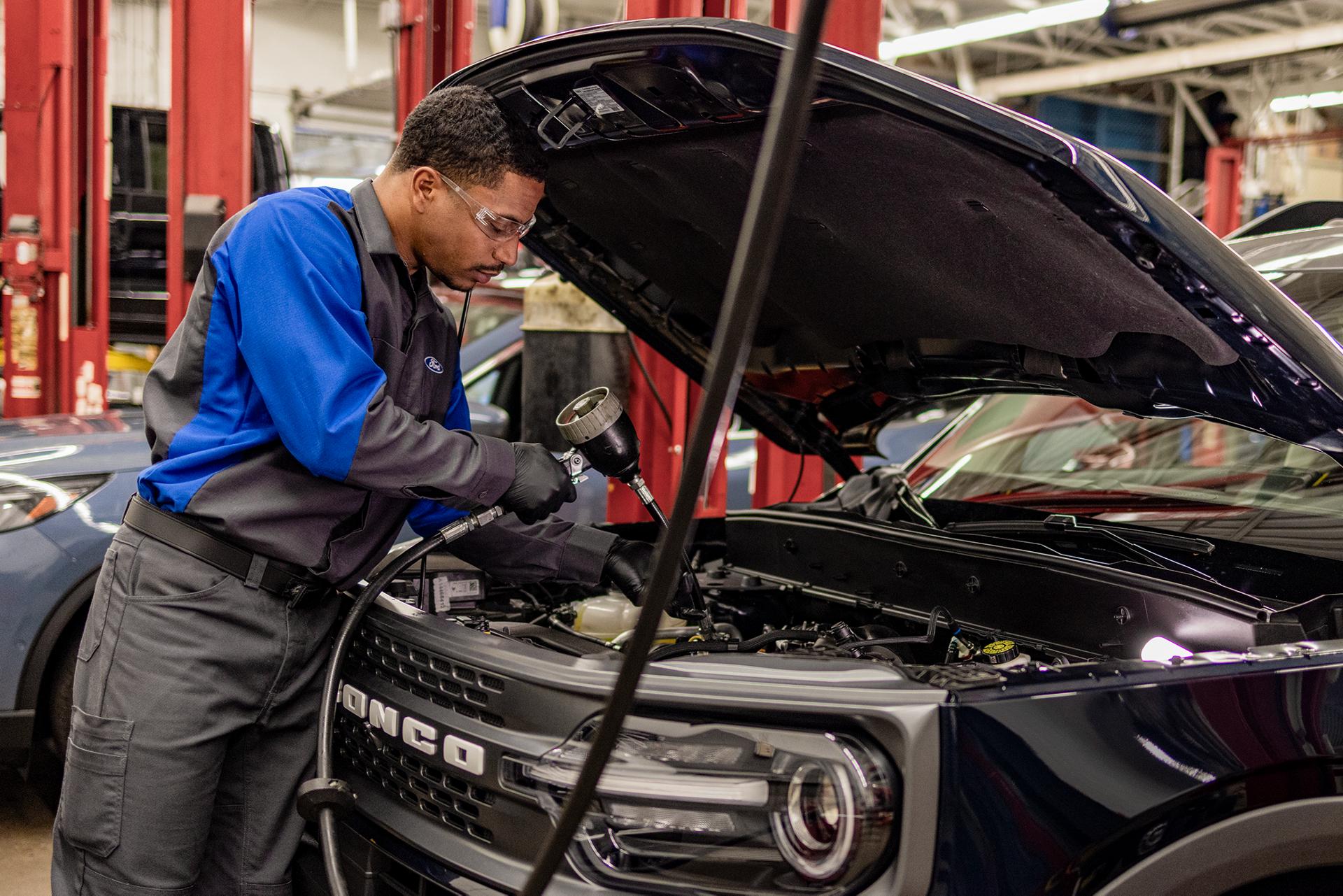 A Ford Service technician changes filling oil in a vehicle in the service bay