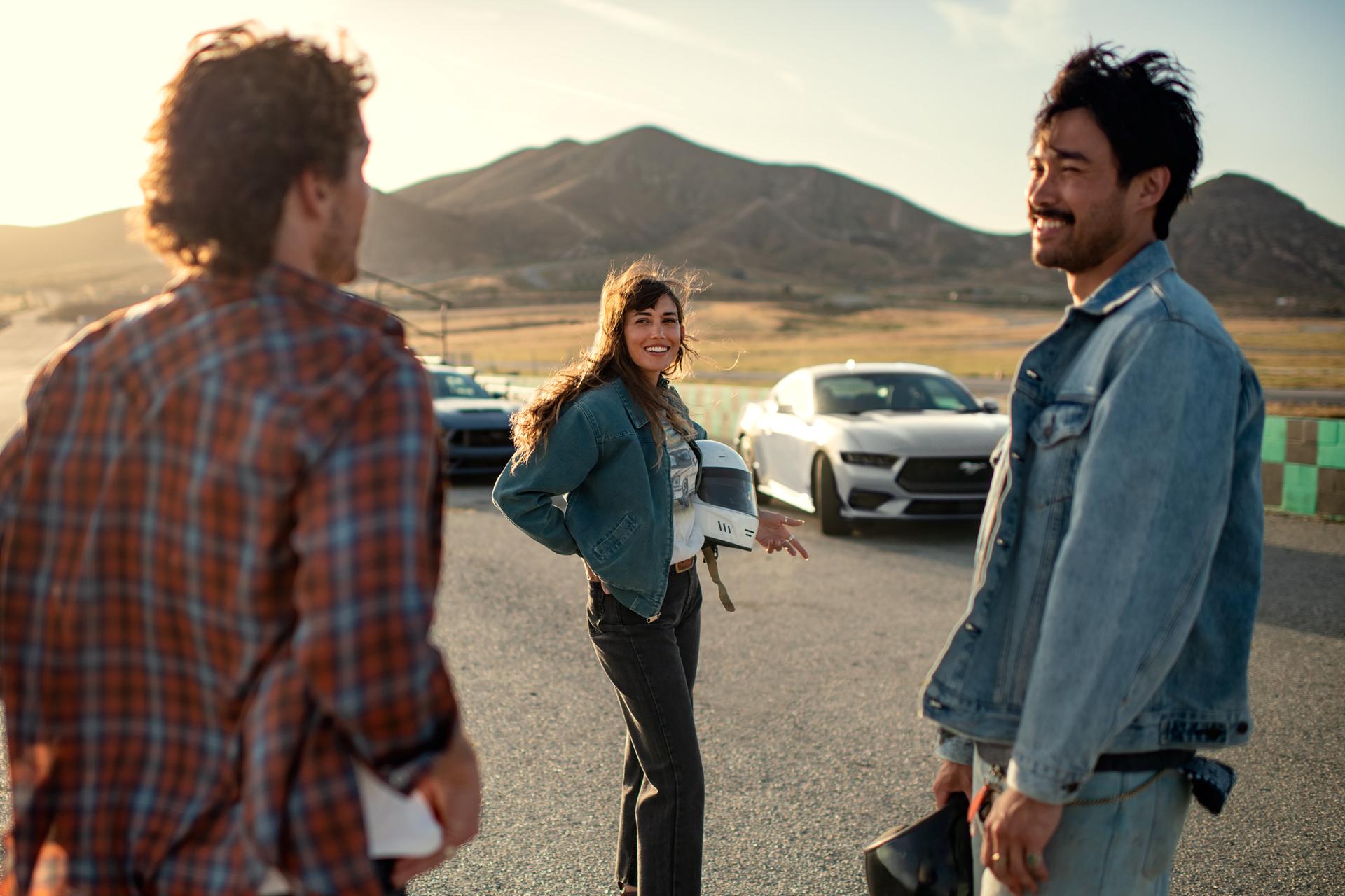 Two 2026 Ford Mustang® fastbacks parked near a race course with three people nearby