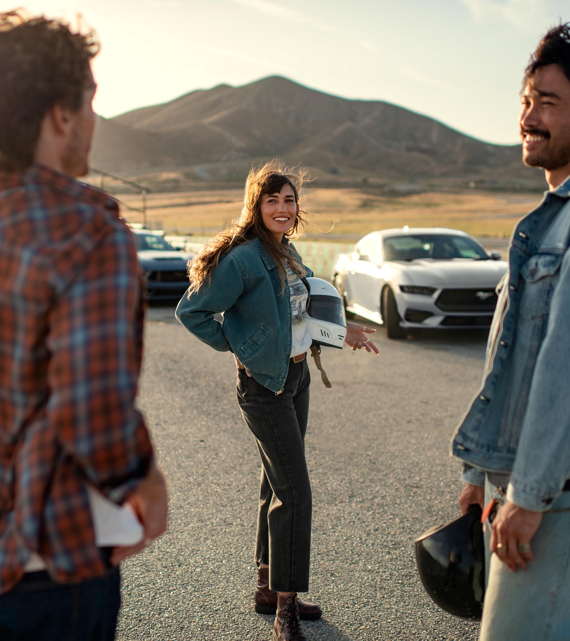 Two 2026 Ford Mustang® fastbacks parked near a race course with three people nearby