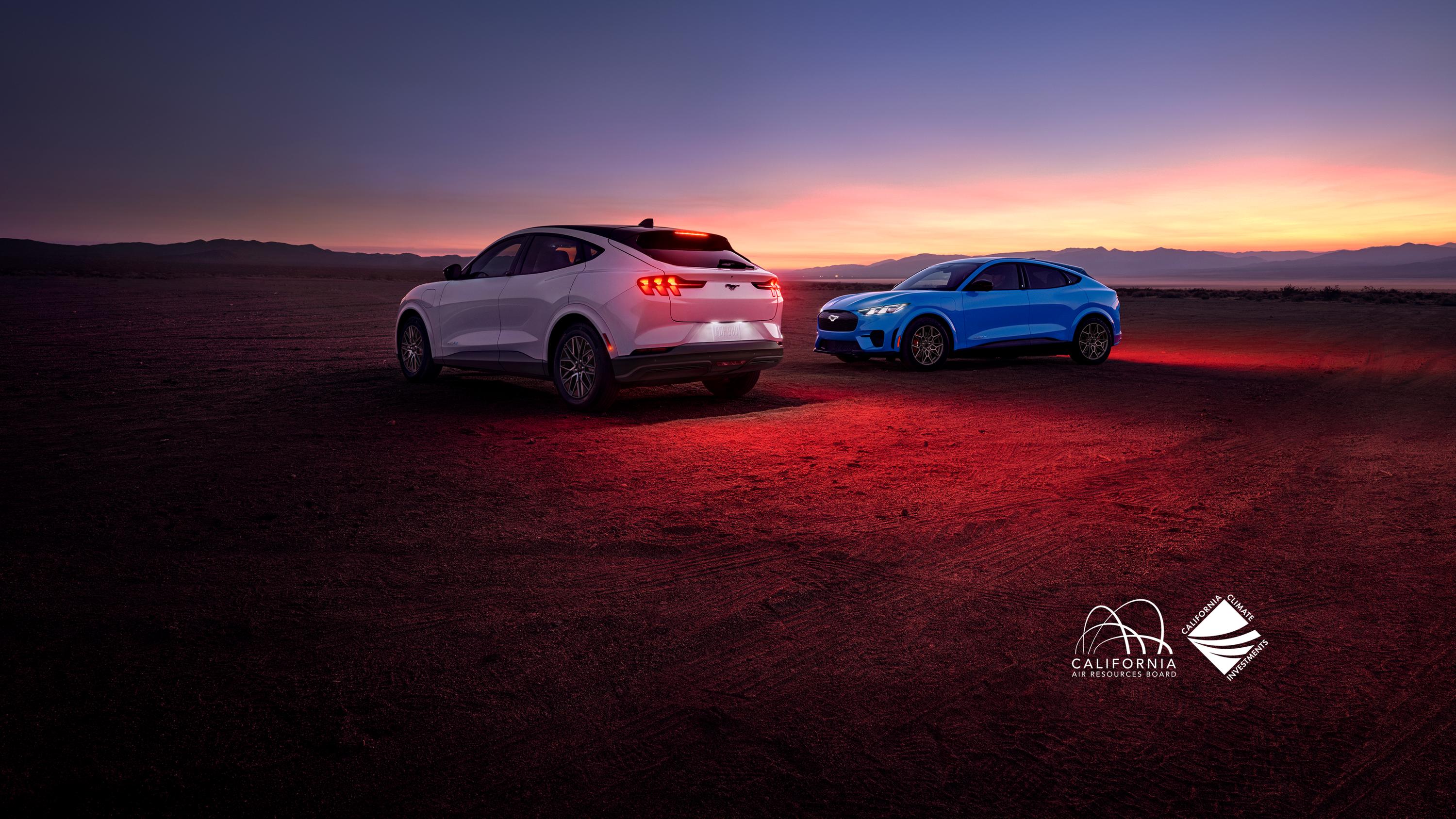 Two Mustang Mach-E vehicles on red dirt with a blue sky above. 