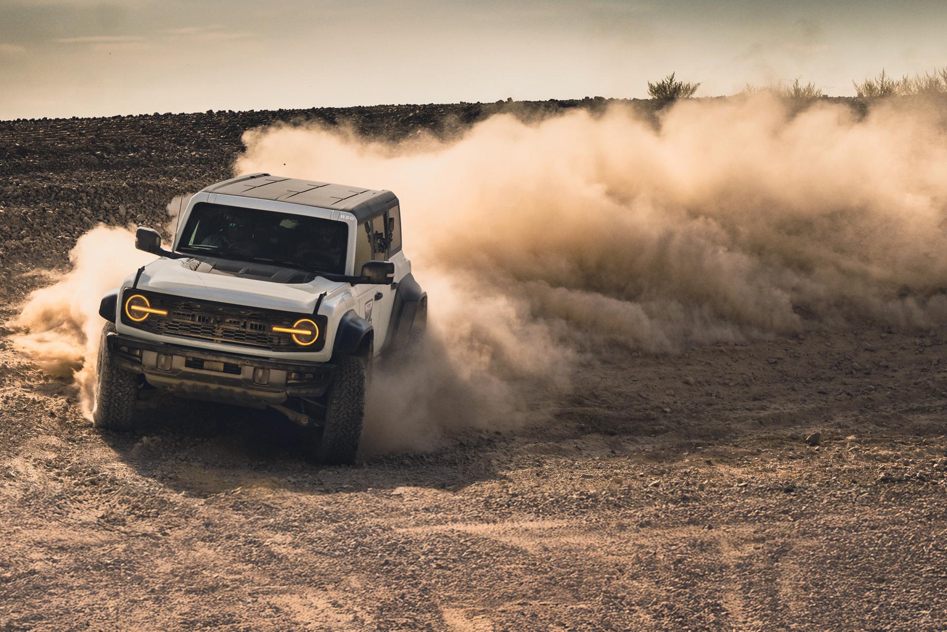 A white 2026 Ford Bronco® using its advanced 4x4 System to execute a safe power slide in the dirt, throwing up a huge dust cloud