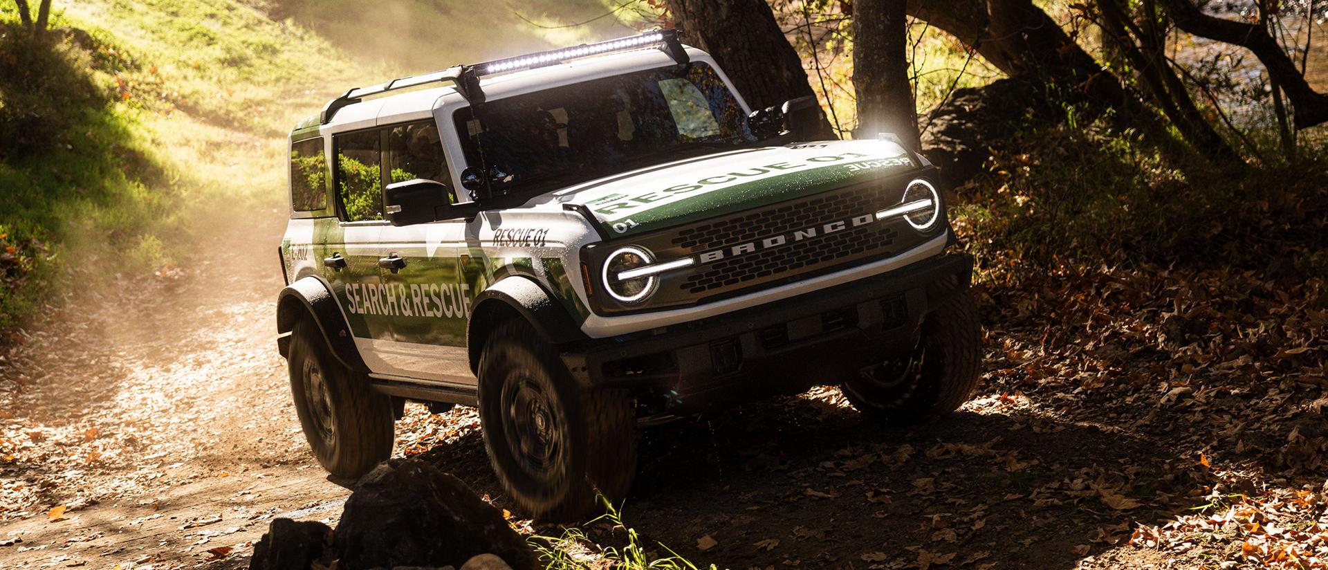 A white with green graphics Ford Bronco Badlands equipped as search and rescue vehicle driving on an incline