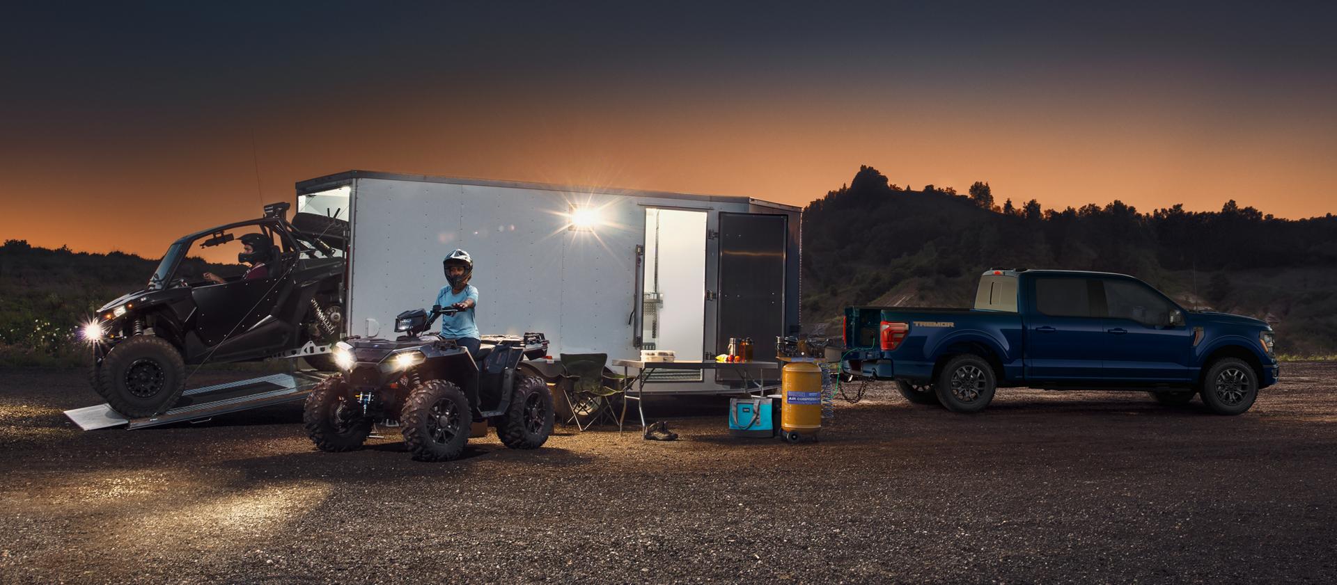 Boy riding an ATV near a 2026 Ford F-150®  Tremor® pickup hitched to a large trailer at night