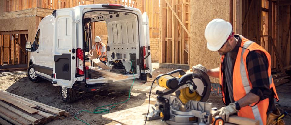 A white 2025 Ford E-Transit™ van parked, rear doors open as a worker uses Pro Power Onboard™ to operate a saw