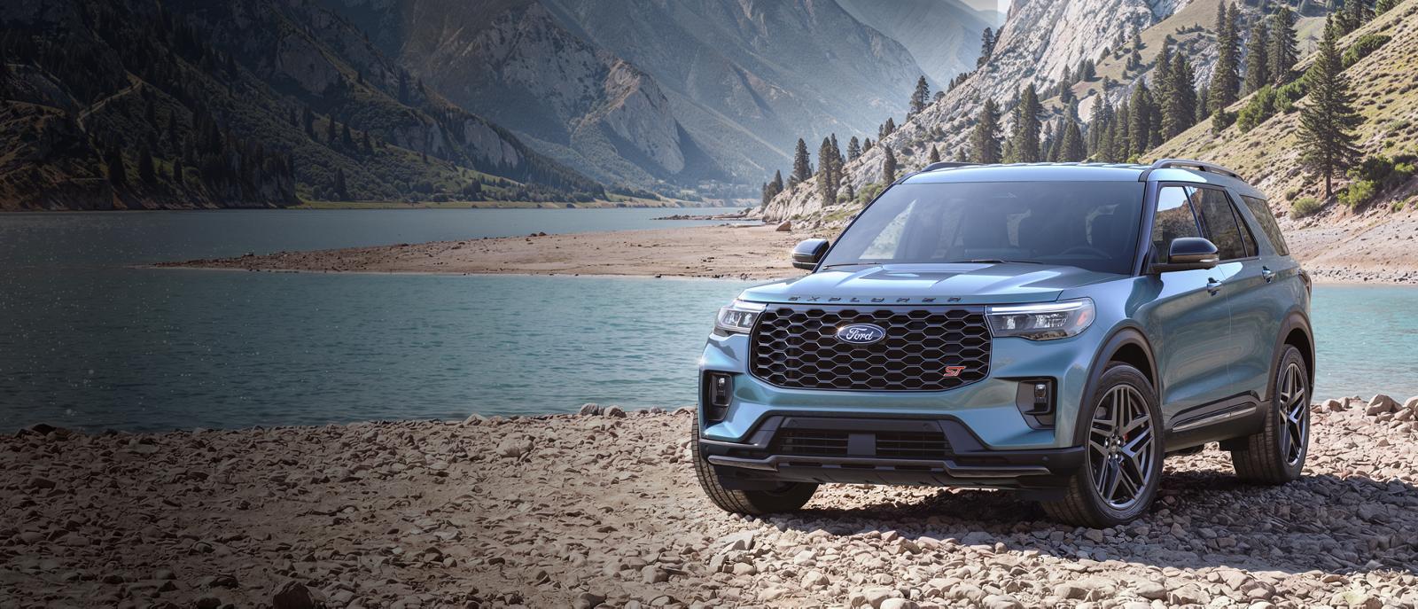 2027 Ford Explorer ST in Vapor Blue parked on rocks beside a mountain lake
