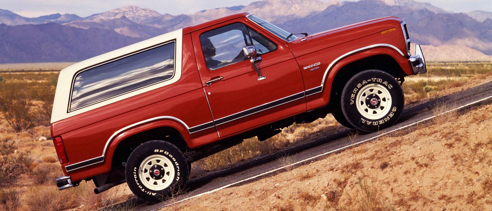 A two-tone 1984 Ford Bronco® model being driven up a steep incline