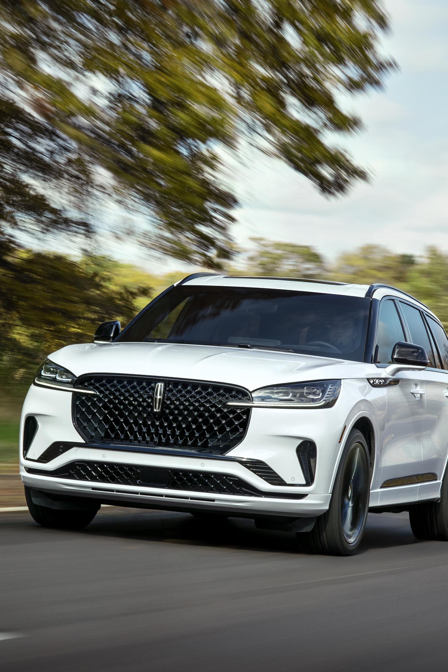 Une Lincoln Aviator 2025 est montrée en train de rouler sur une route dans la forêt.