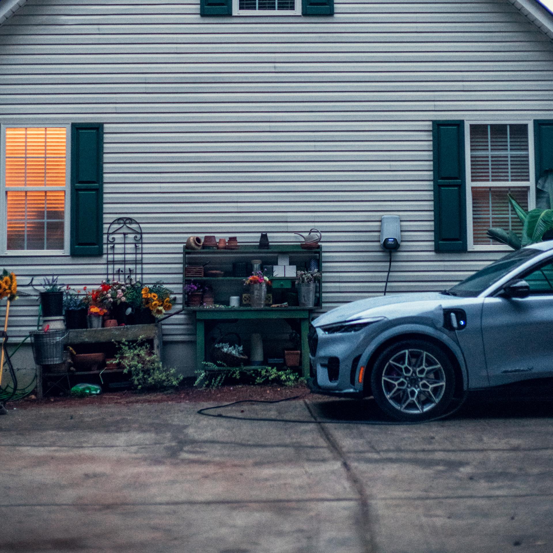 Ford Mustang Mach-E® parked in a driveway and plugged into home charger attached to the side of a house