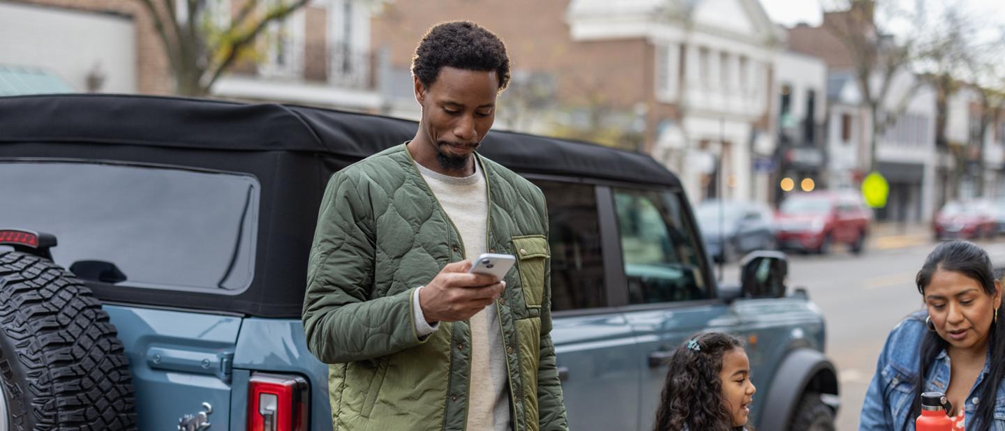 A man looks at his phone while standing beside his Ford Bronco®