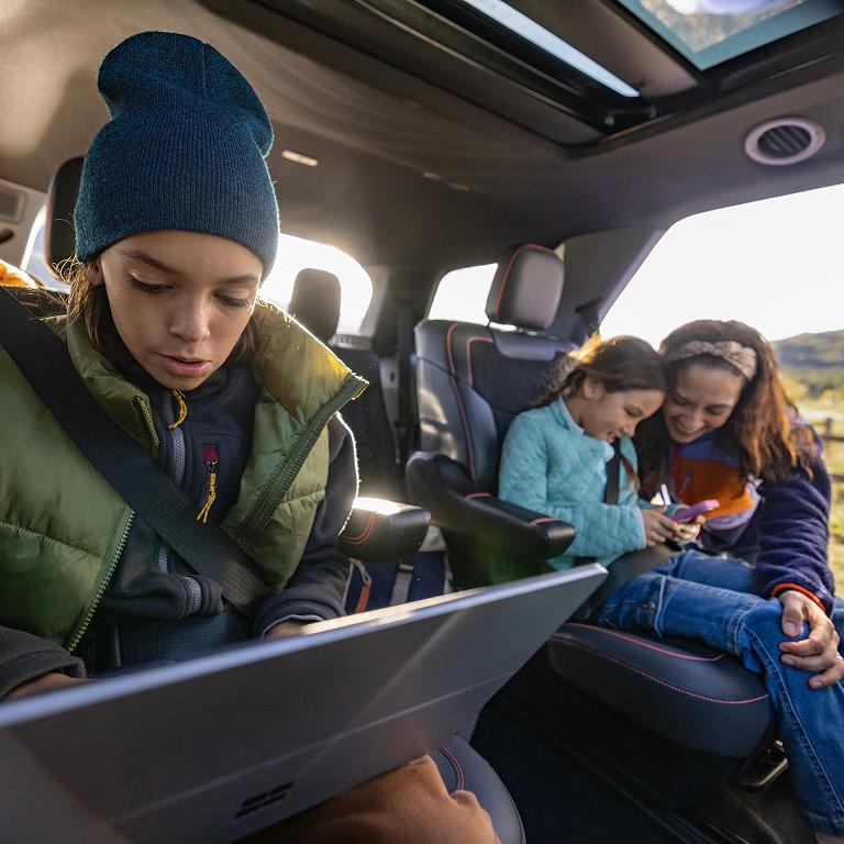 A husband and wife looking at a tablet from the open rear hatch of a parked Ford Expedition.