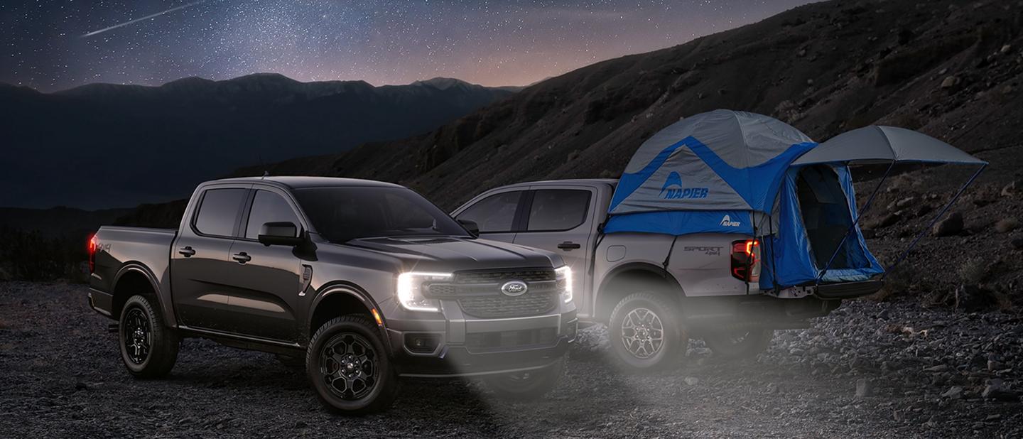 Two 2026 Ford Ranger® trucks parked under a starry, nighttime sky. One of them with a tent in the truck bed