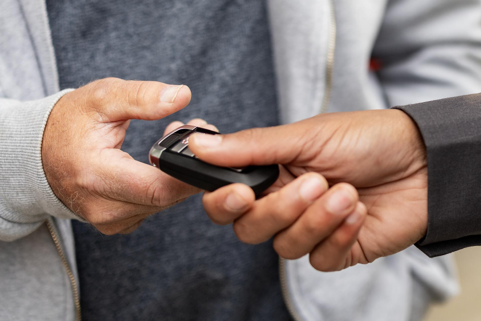 A Ford key fob is handed from a Ford dealer to a proud new owner
