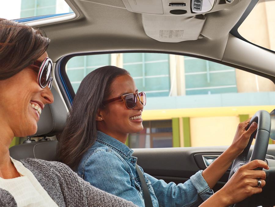 Two women, both wearing sunglasses, sitting in the front seats of a Ford vehicle.