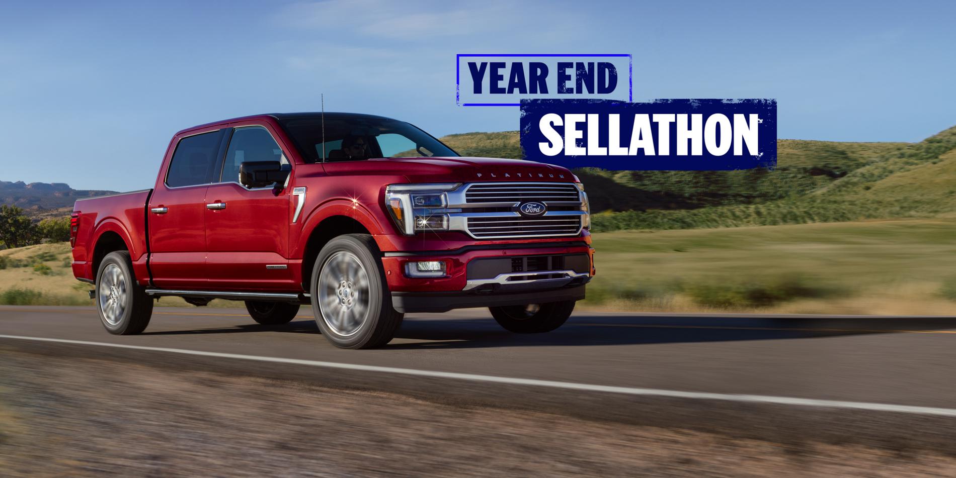 A red 2025 Ford F-150® truck being driven on a rural highway with rolling hills in the background.