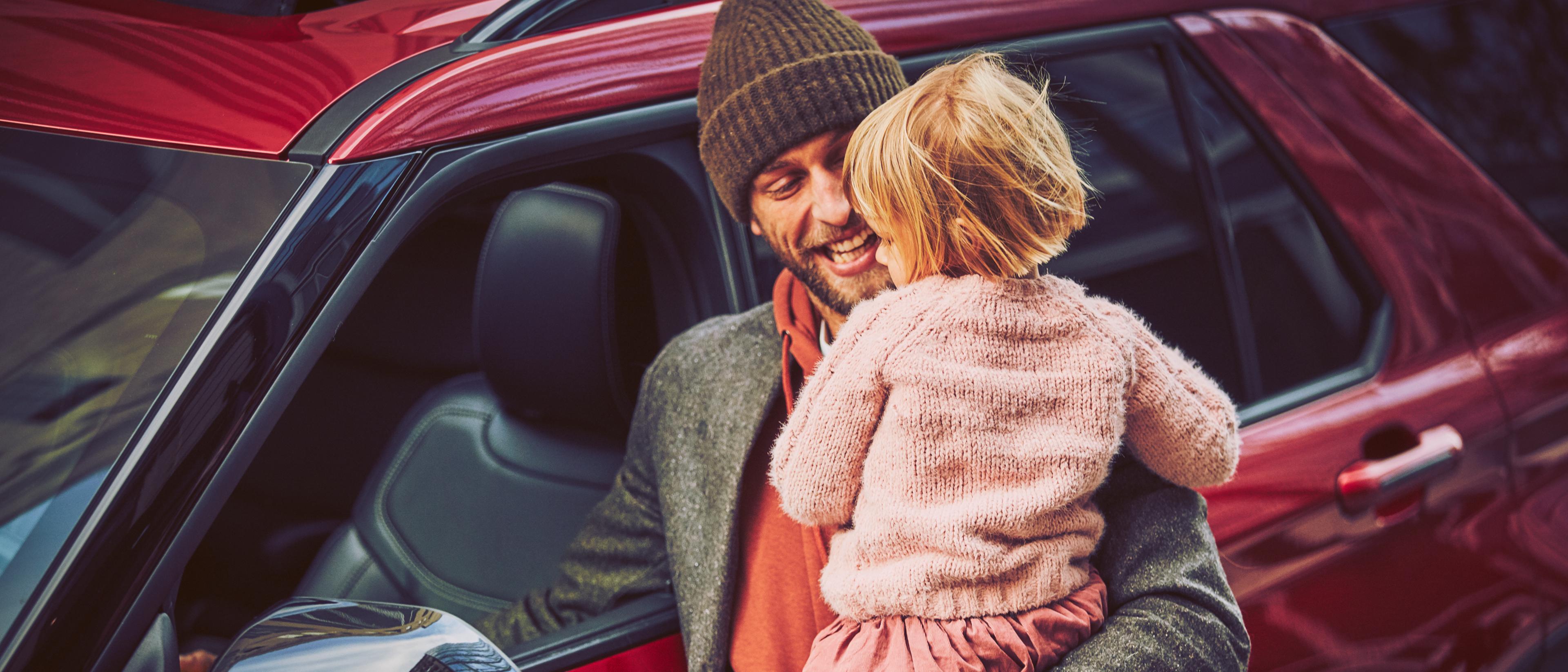 A father smiles widely while holding his child, walking around the Ford Explorer® SUV