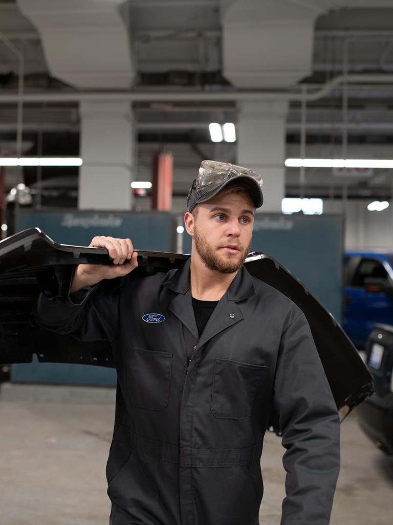 Collision repair person carrying car bumper in shop