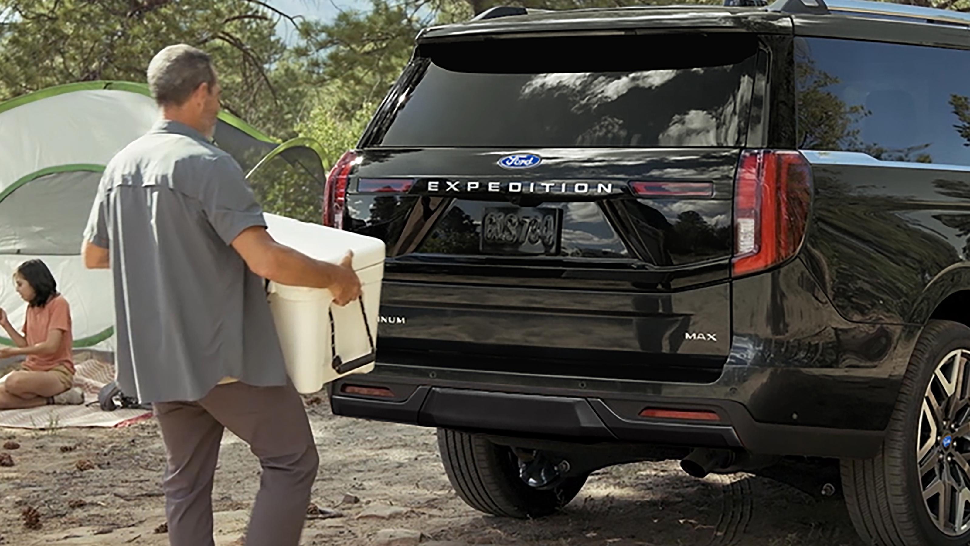 Person using the Ford Split Gate with available Open On Approach to load a cooler in a 2027 Ford Expedition® SUV