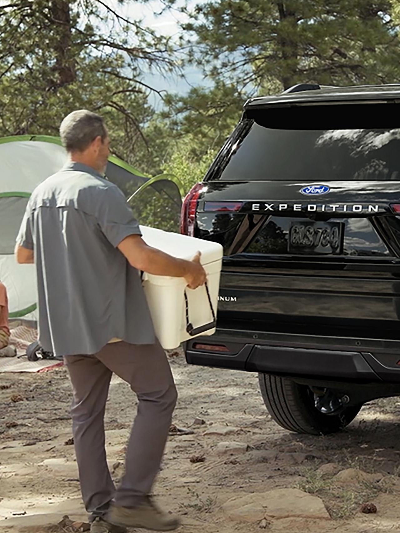 Person using the Ford Split Gate with available Open On Approach to load a cooler in a 2027 Ford Expedition® SUV