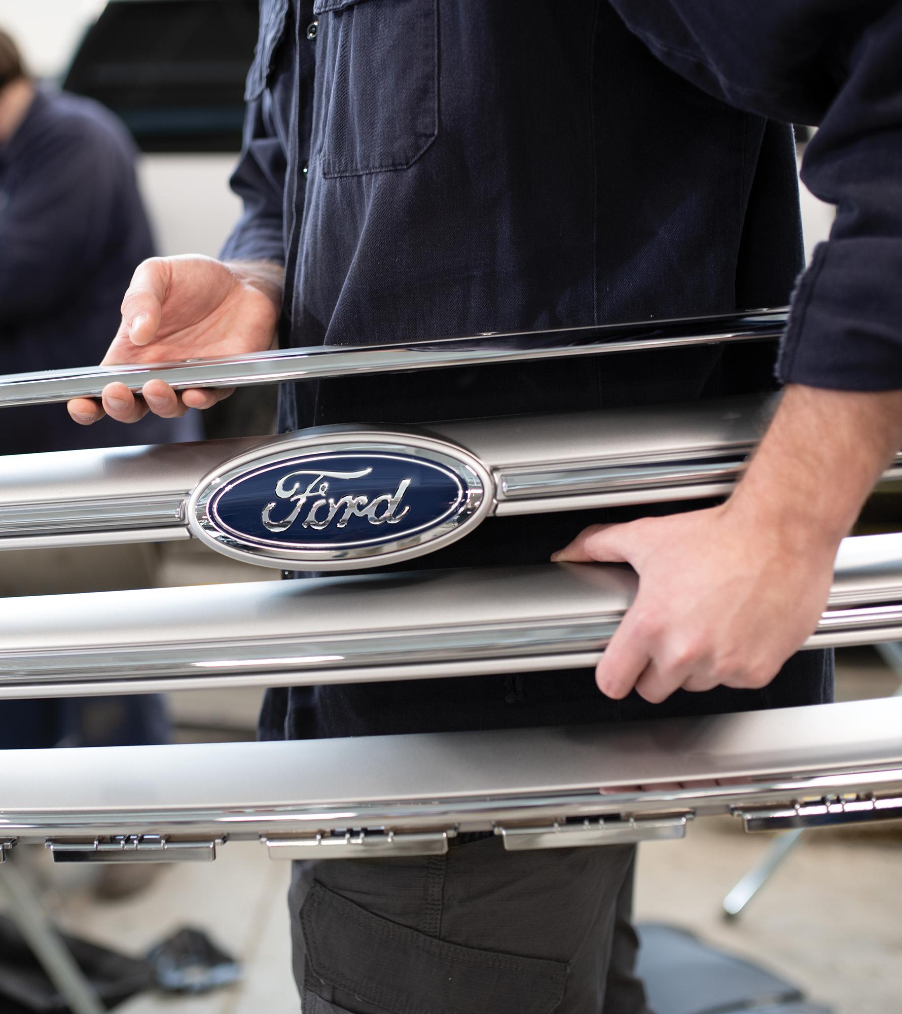 Service technician carrying a vehicle’s front grill in repair shop