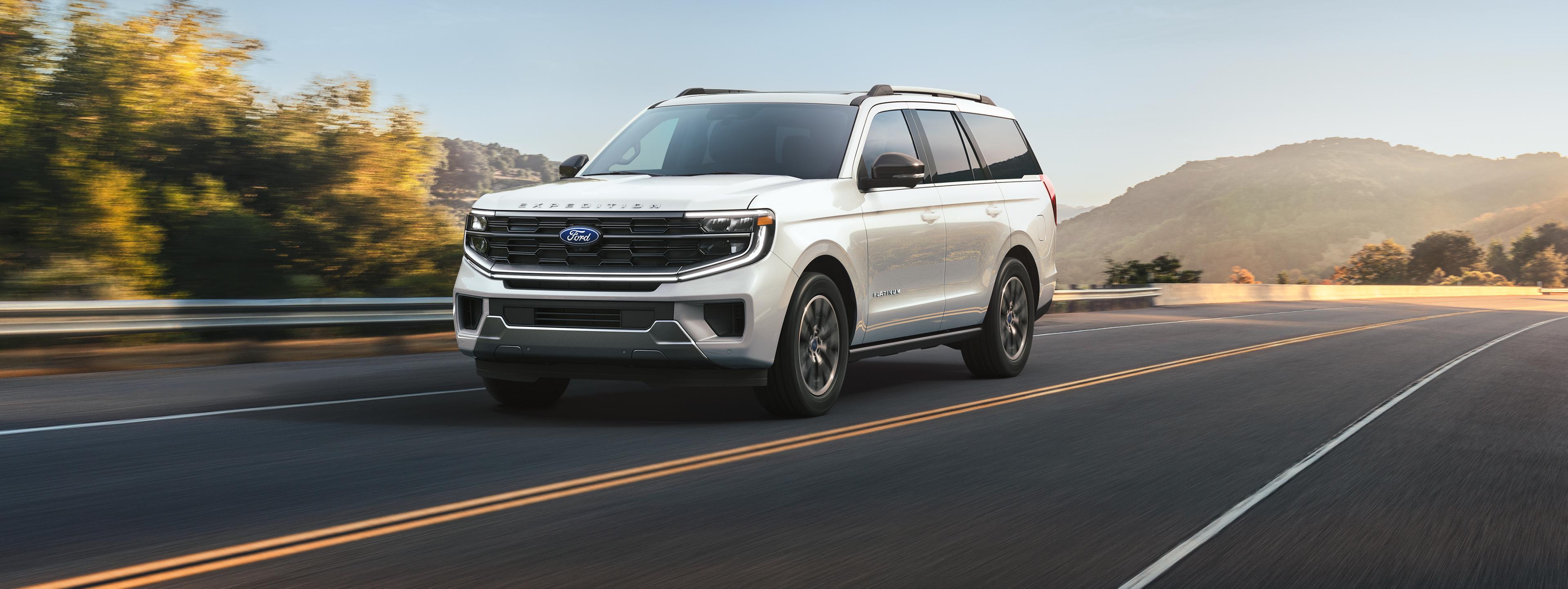A white 2025 Ford Expedition driving down a road with mountains in the background