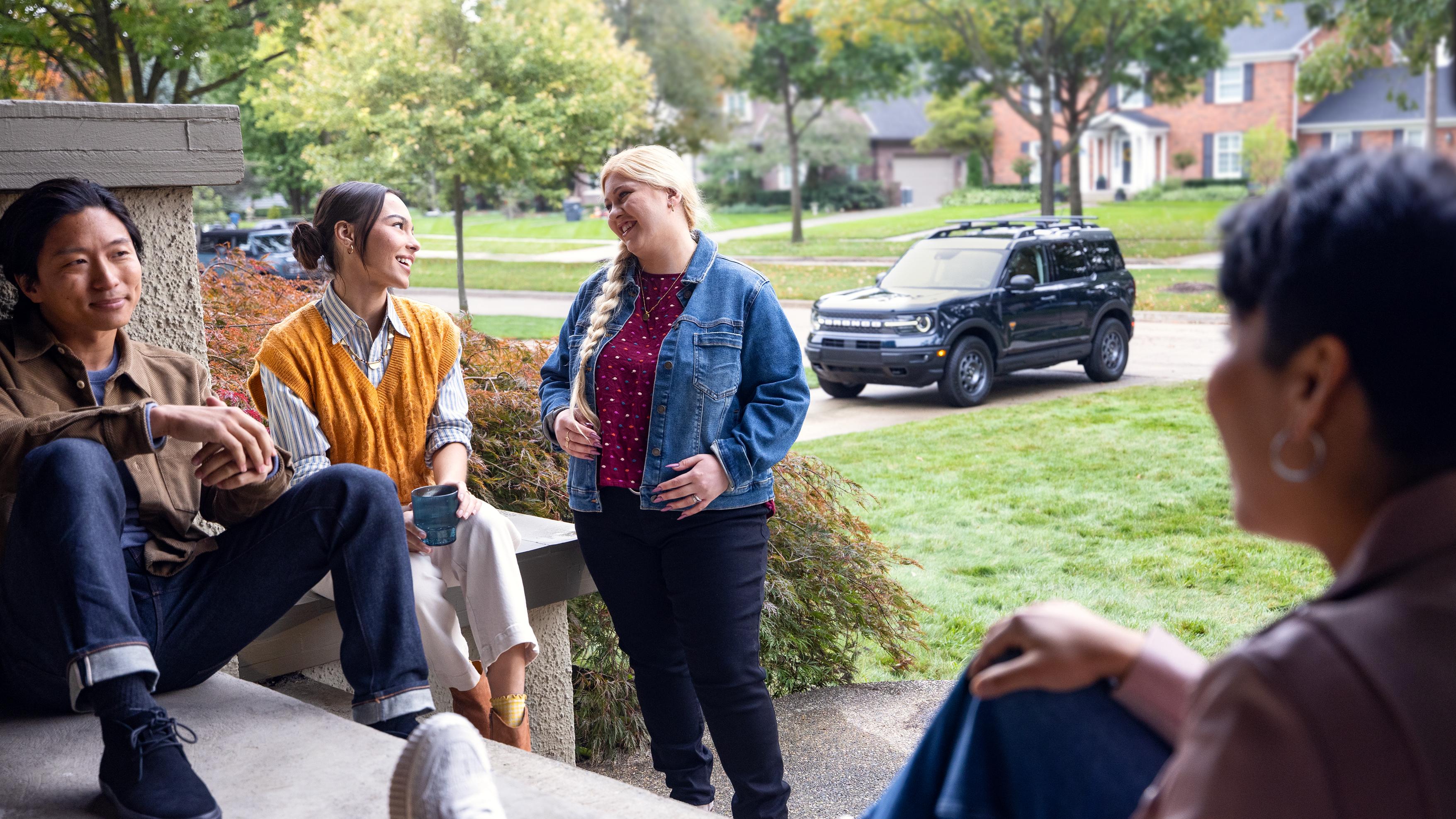 A group of friends gather on a porch with a Ford Bronco Sport® SUV parked in the driveway behind them