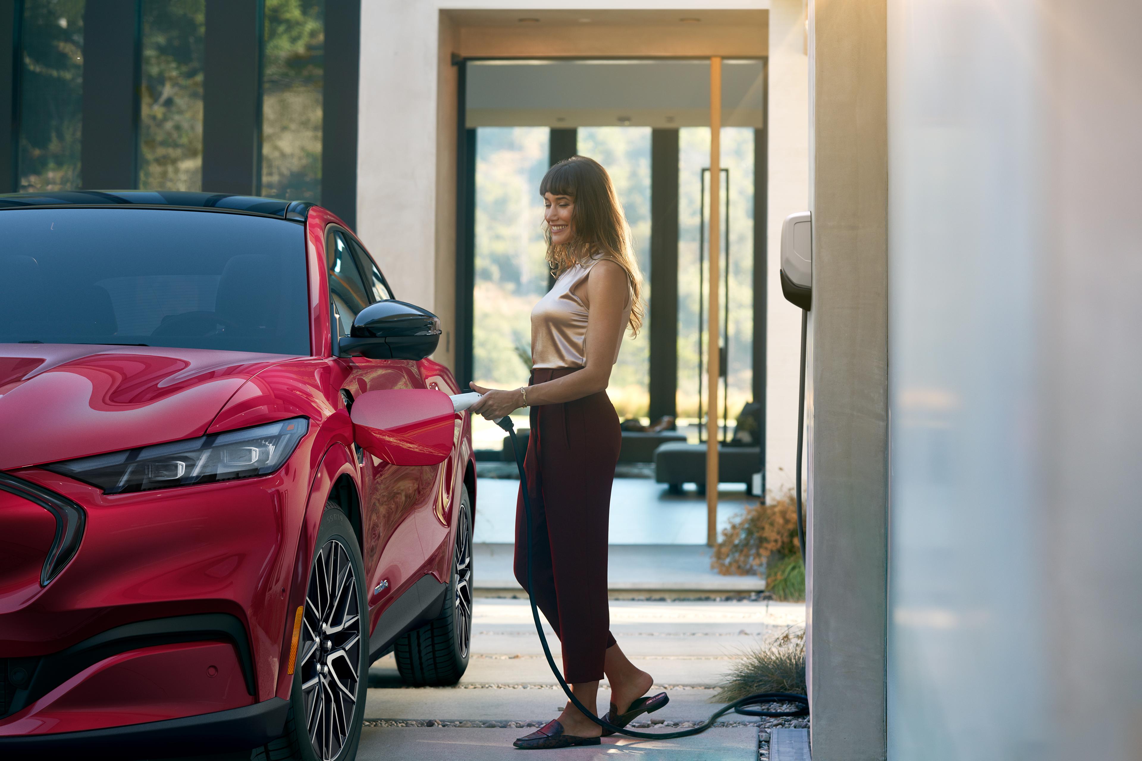 Woman plugs in a 2025 Ford Mustang Mach-E® parked outside a home