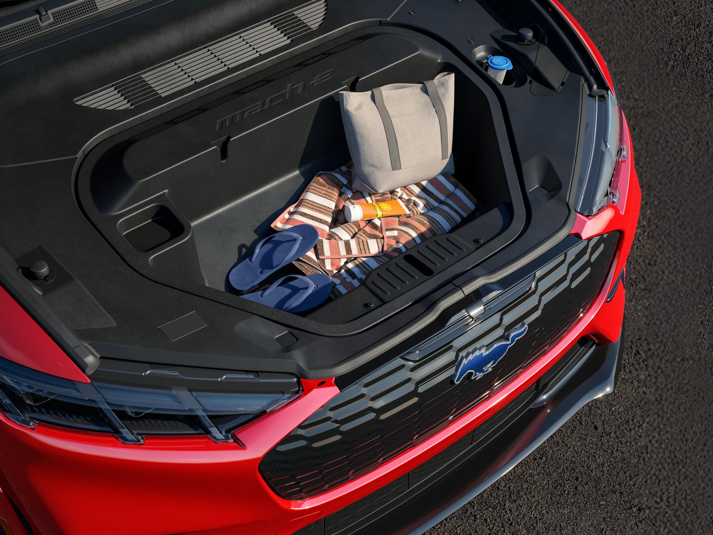 An open front trunk (frunk) of a red 2026 Ford Mustang Mach-E® SUV packed with beach gear