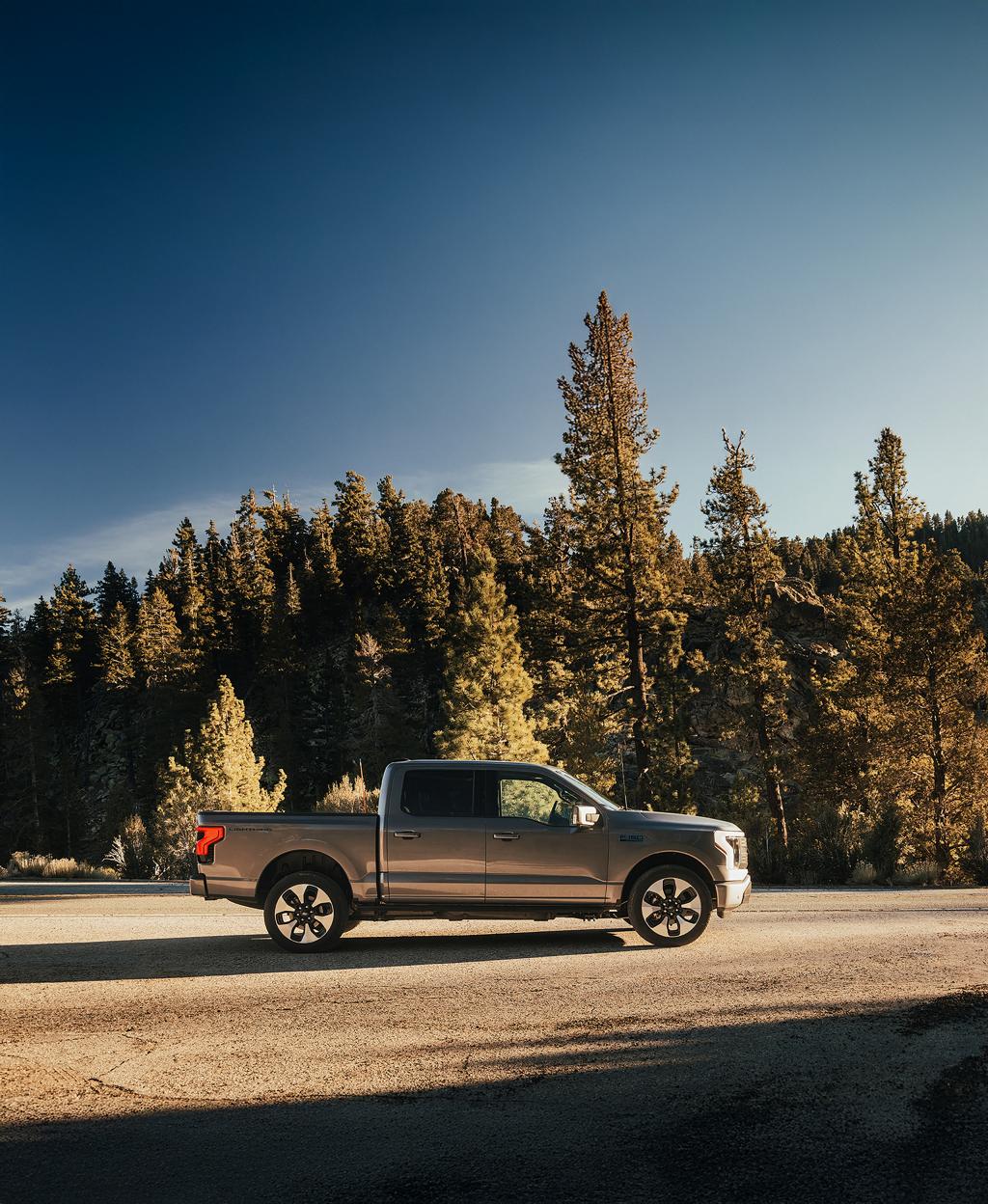 A 2025 Ford F-150® Lightning® in Iconic Silver parked on a paved road showing off the side profile