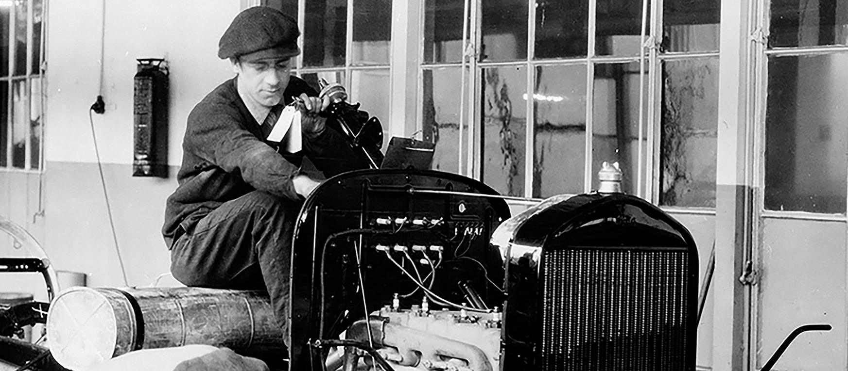 Black and white photo of two men working on a car assembly line