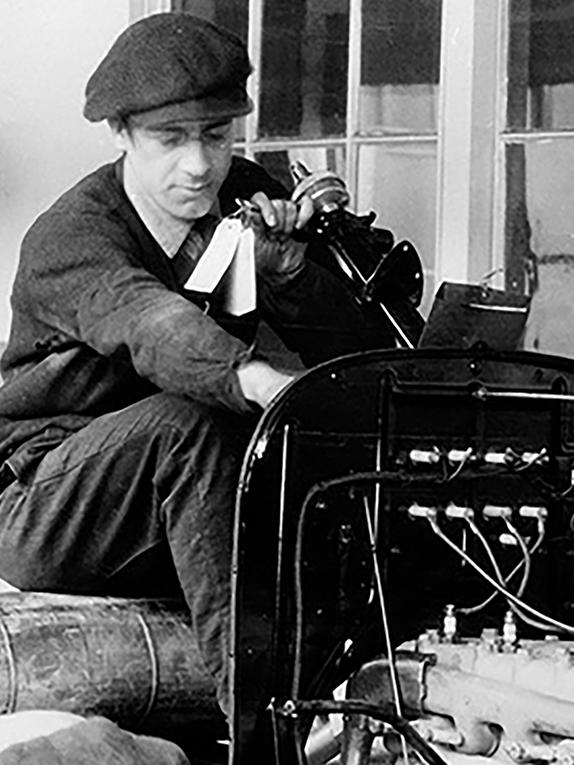 Black and white photo of two men working on a car assembly line