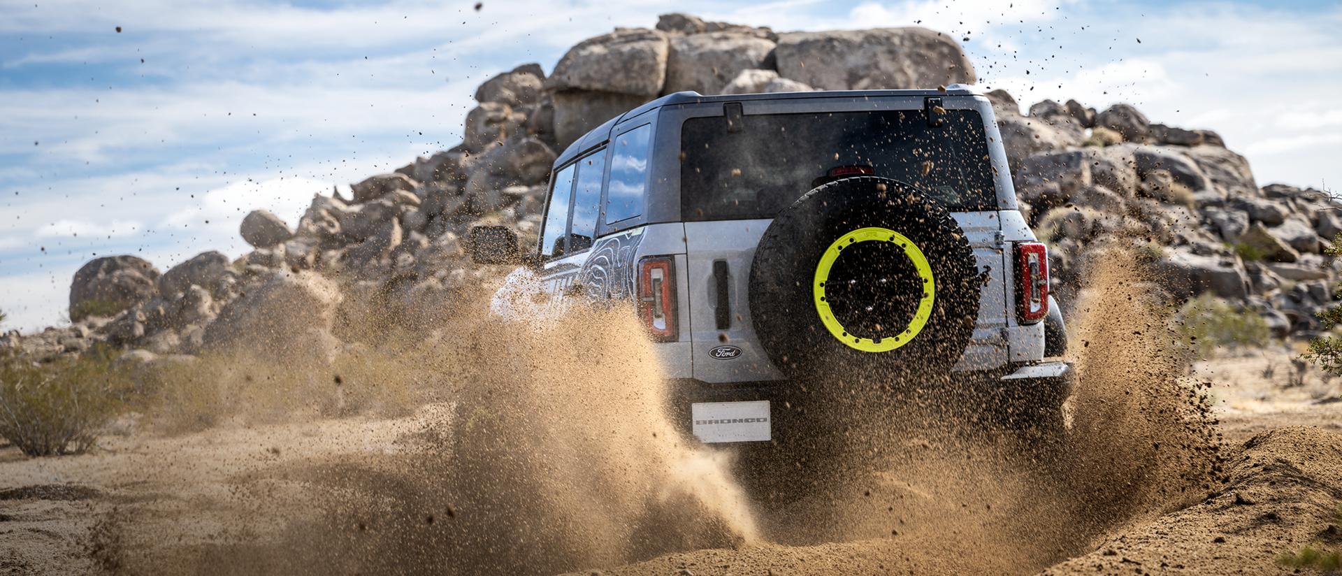 A 2027 Ford Bronco® RTR model kicking up dirt near a large rock pile