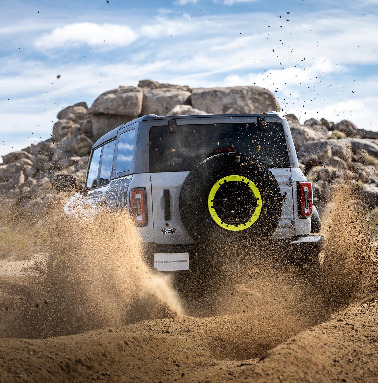 A 2027 Ford Bronco® RTR® model kicking up dirt near a large rock pile