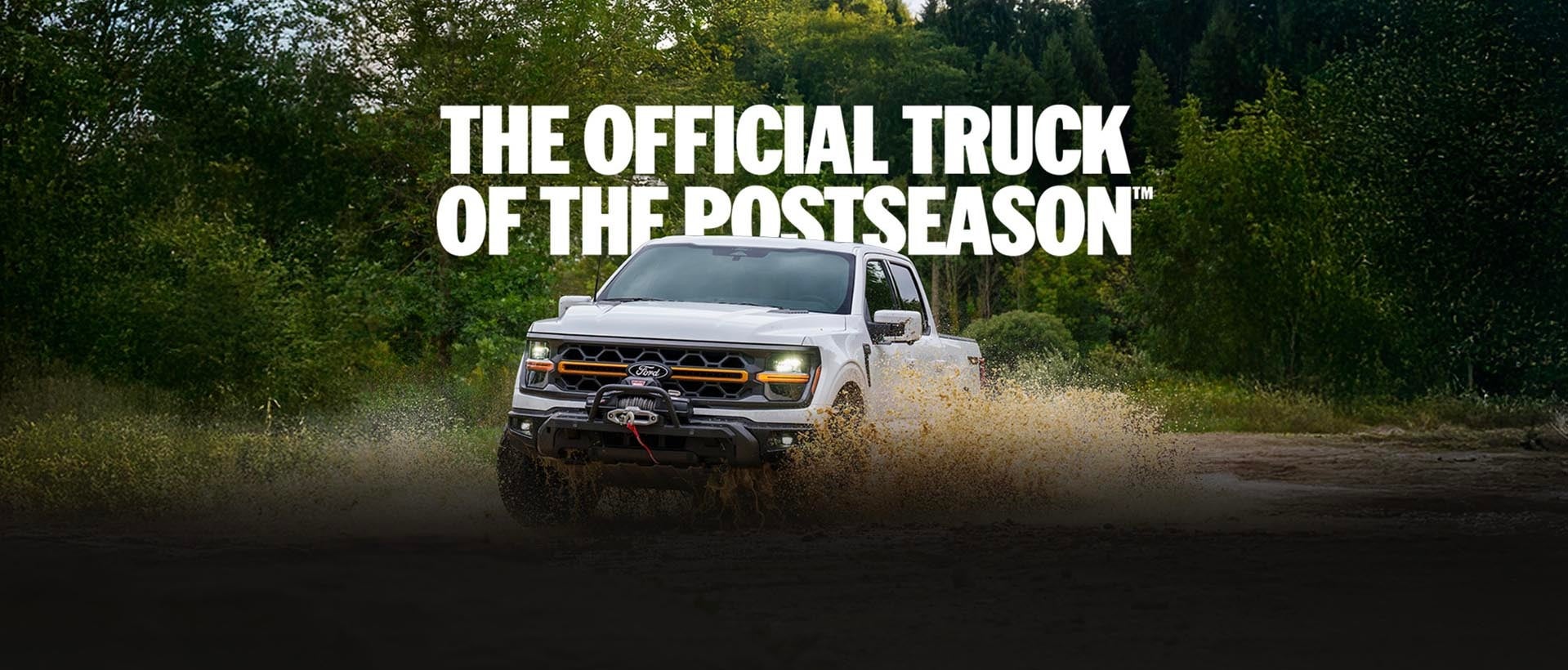 White 2026 Ford F-150® truck driving through a muddy puddle on an off-road forest trail