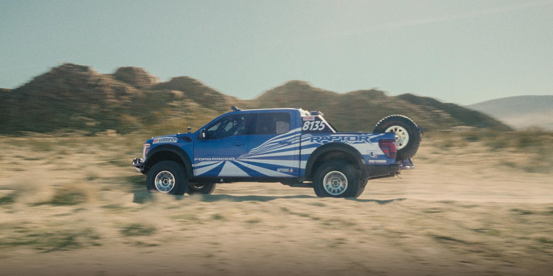 A blue with white graphics 2025 Ford Ranger® Raptor® driving through muddy terrain