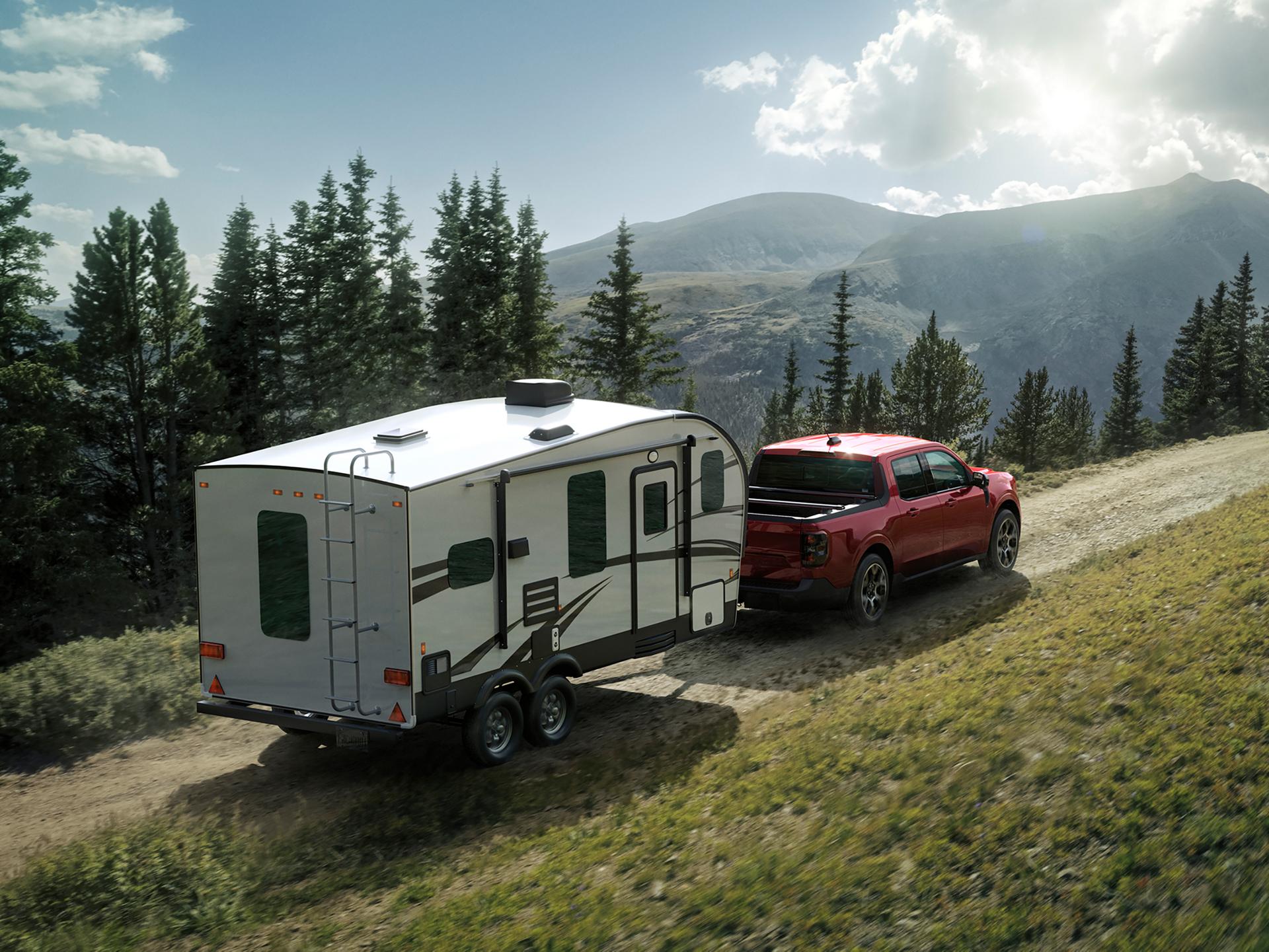 2026 Ford Maverick® Lariat pickup in Ruby Red Metallic Tinted Clearcoat (extra cost) pulling a camper on a mountain pass