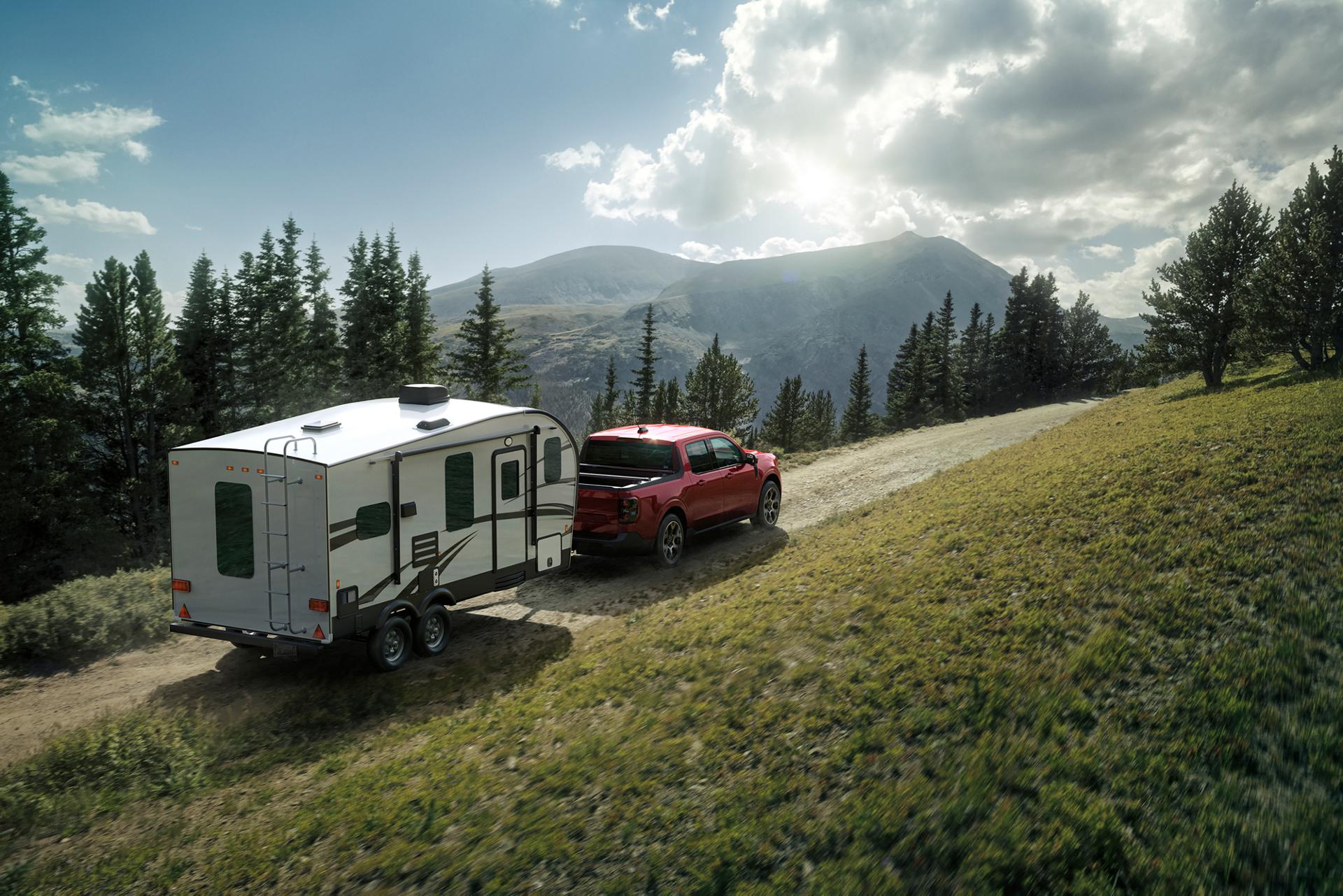 2026 Ford Maverick® Lariat pickup in Ruby Red Metallic Tinted Clearcoat (extra cost) pulling a camper on a mountain pass