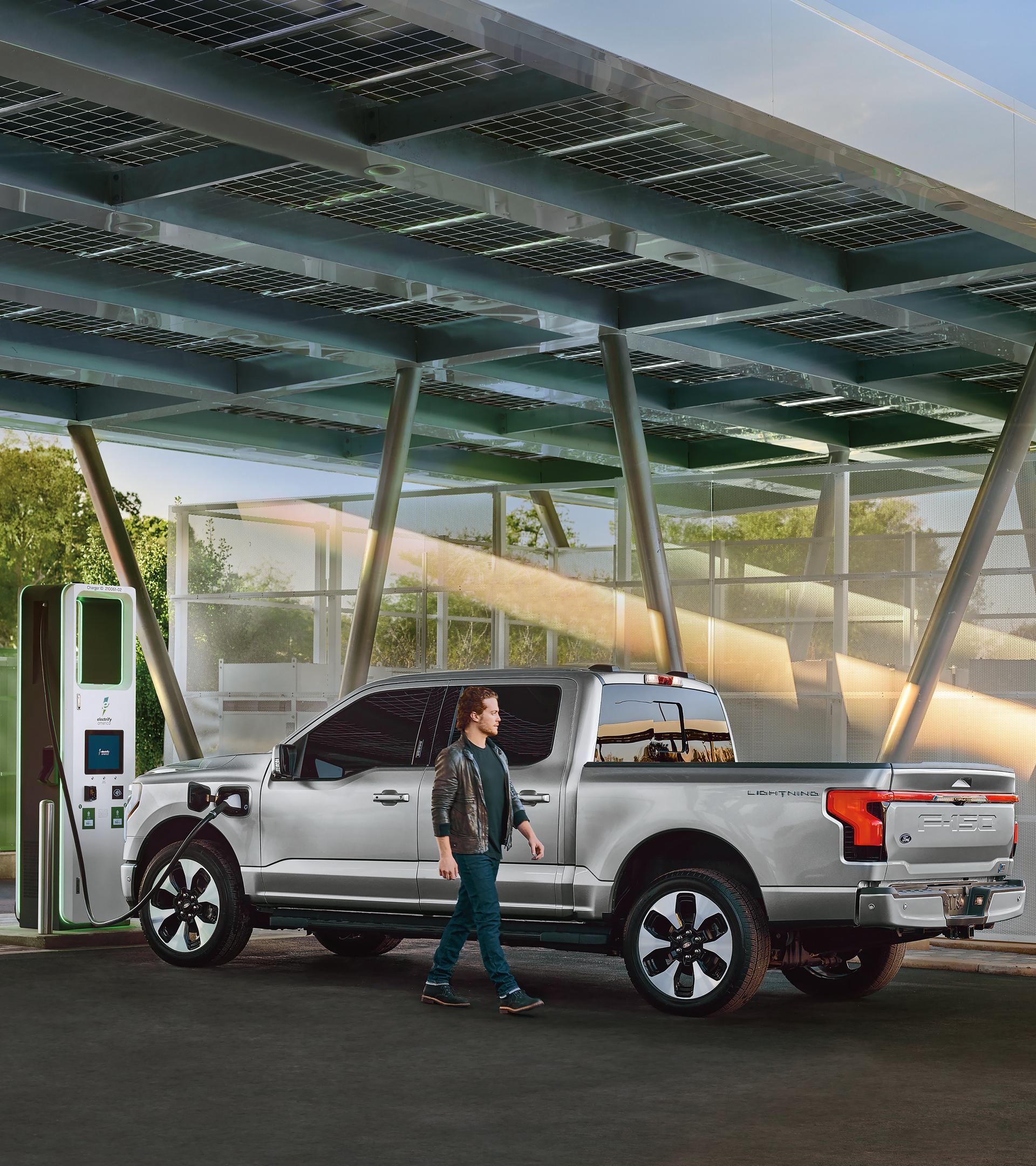 Person walks by a parked F-150 Lightning connected to a public charging station.