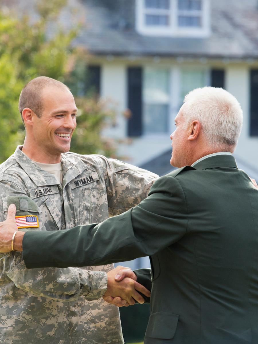 A man in military fatigues hugs his father wearing a military dress uniform