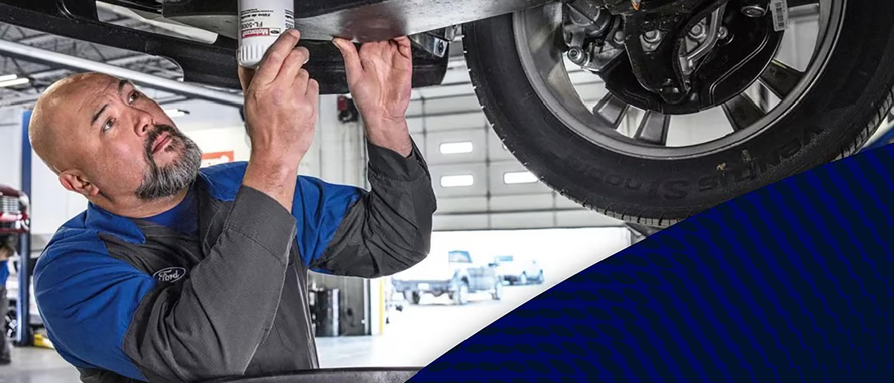 A Ford mechanic tightens the oil filter on a Ford vehicle hoisted up on the lift