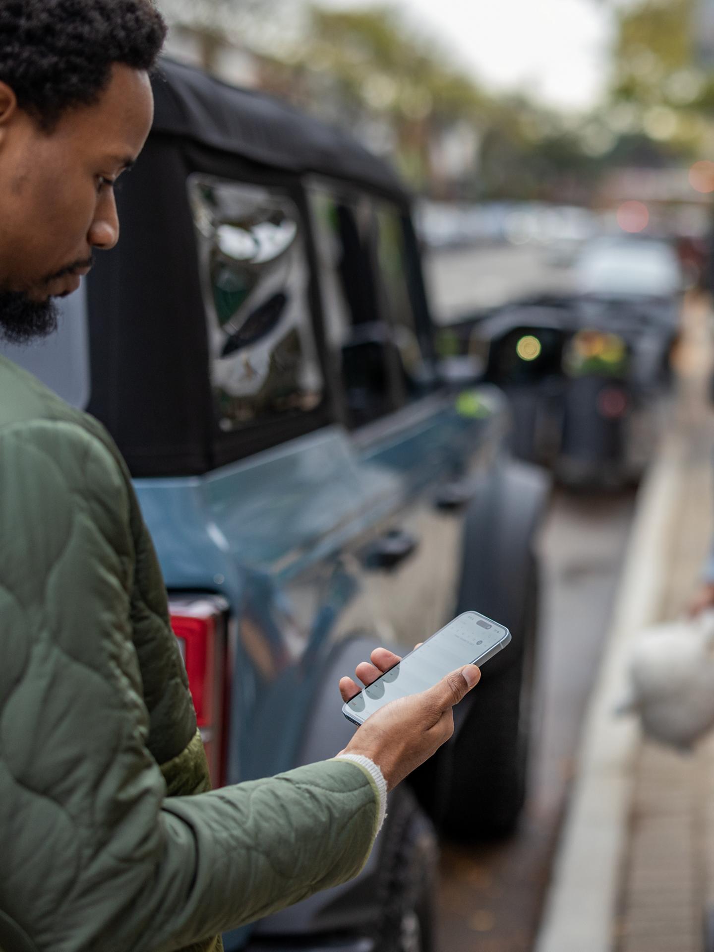 A Ford Bronco® SUV owner glances at their phone outside their vehicle