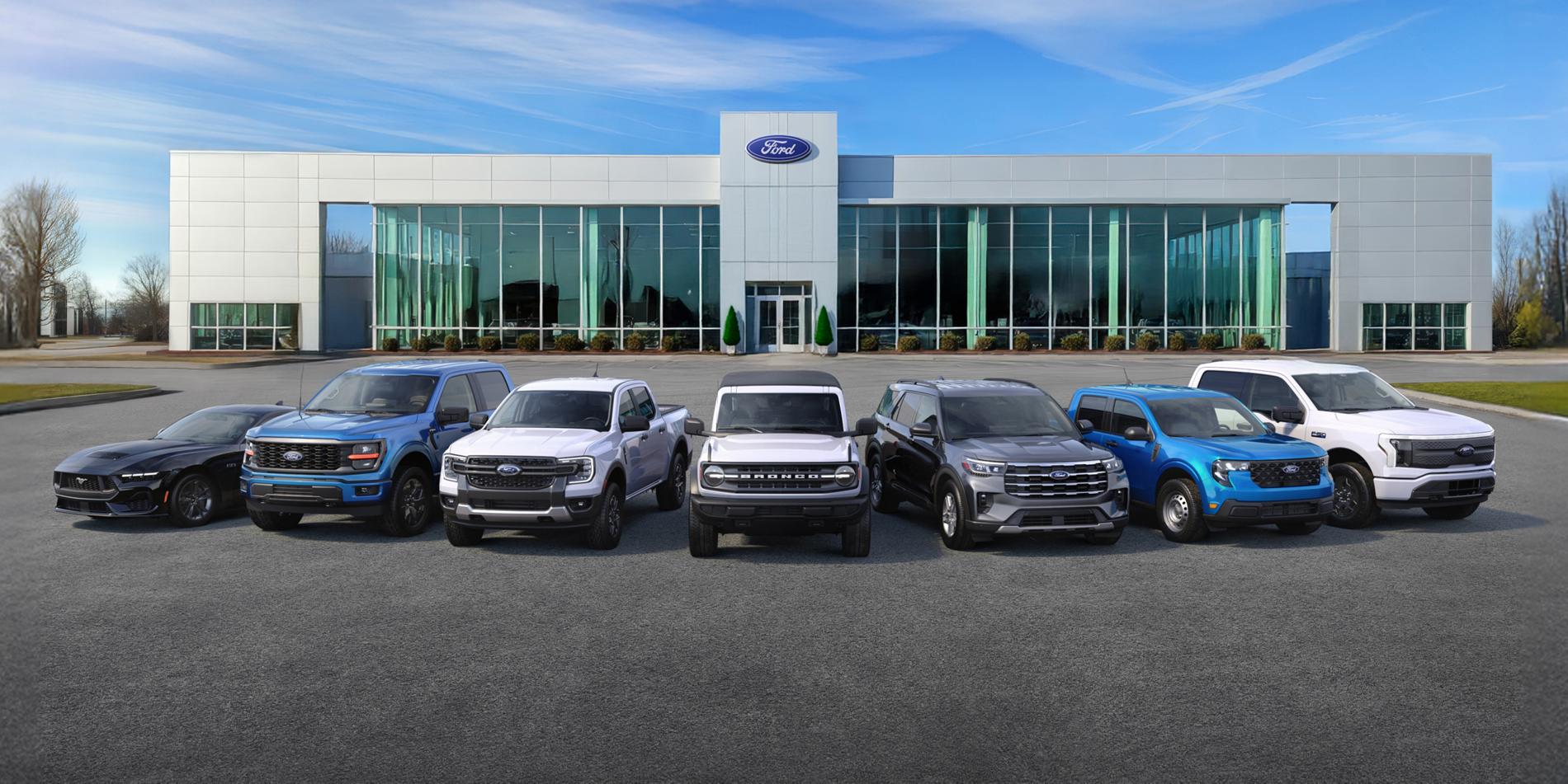 A full lineup of Ford vehicles arranged in front of a Ford dealership. A Ford Ranger, Ford Bronco and Ford Explorer are in the center.